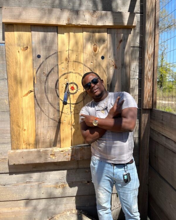 Gentleman standing next to axe stuck at the Timber Creek Distillery axe throwing range.