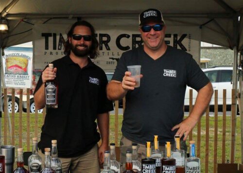 Cam and Aaron holding a bottle of whiskey and a drink at an event