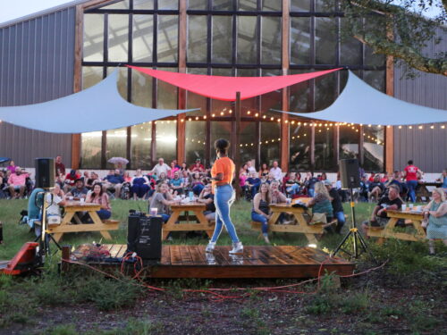 behind the comedian looking at the window wall with the crowd and cafe lights.