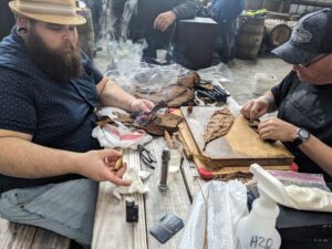 A cigar rolling experience at Timber Creek Distillery. A gentleman is about half way through rolling a cigar. the wrapper leaf is laid out on a wooden cutting board.