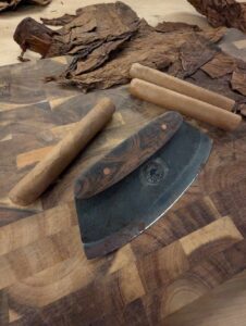 cigar with loose tobacco and chaveta on wooden cutting board